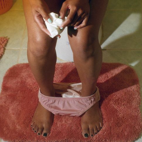 view of woman's legs on toilet holding tissue