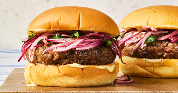 burgers topped with fresh herbs and pickled onions on cutting board
