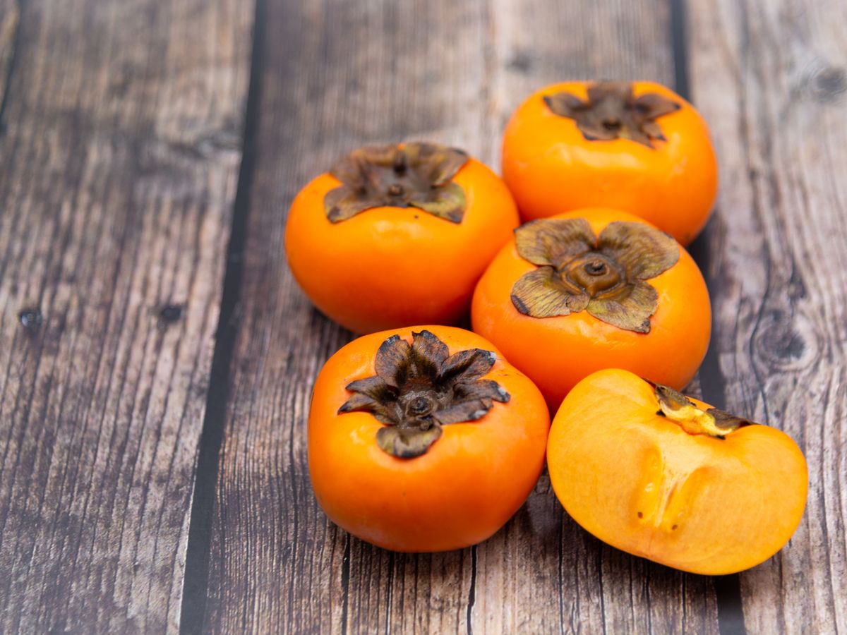 https://hips.hearstapps.com/hmg-prod/images/persimmon-fruit-on-old-wooden-background-top-view-royalty-free-image-1651607677.jpg?crop=0.88097xw:1xh;center,top&resize=1200:*