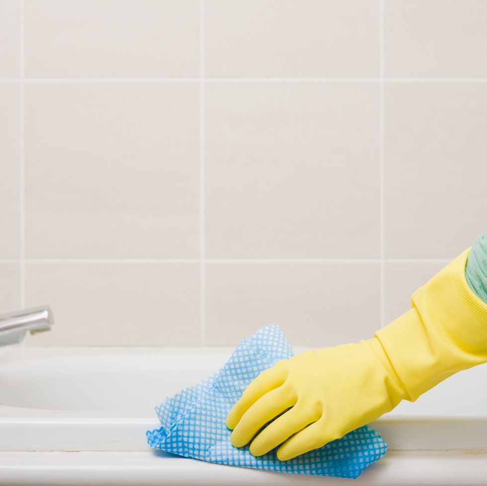 person cleaning bath with rubber gloves