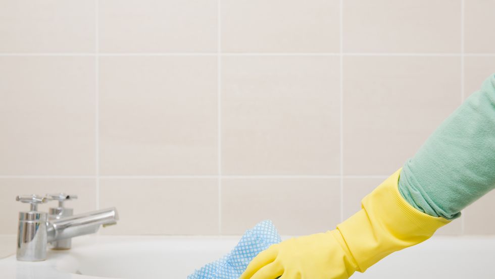 person cleaning bath with rubber gloves