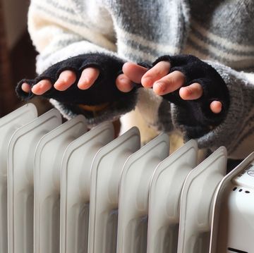 person heating their hands at home over a domestic portable radiator in winter