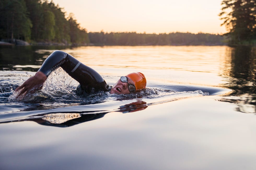 Individual swimming in outdoor waters wearing a wetsuit and swim cap