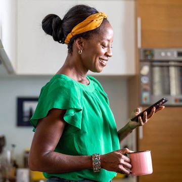 a person looking at their phone while holding a mug in a kitchen