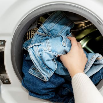 person putting jeans into the drum of a washing machine, front view. washing dirty jeans in the washer