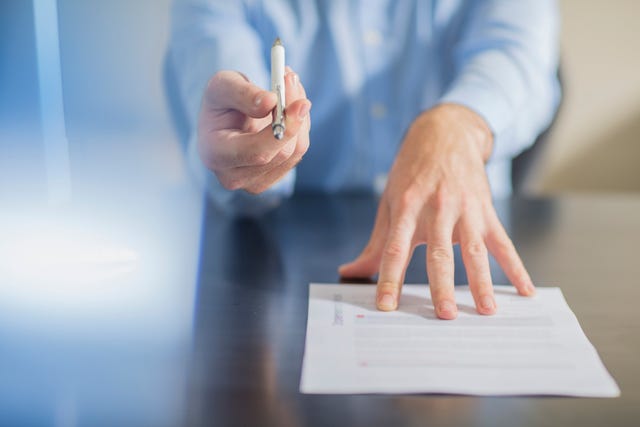 Person sitting at office desk presenting ballpen and contract
