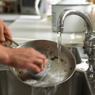 person washing a dirty frying pan under a kitchen sink tap