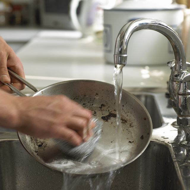 person washing a dirty frying pan under a kitchen sink tap