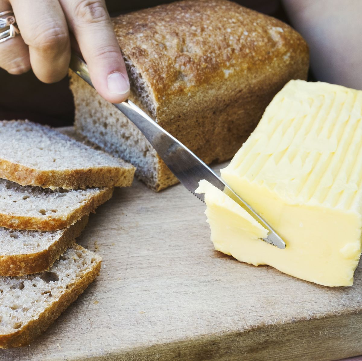 A person with a knife slicing through a block of butter for a sliced bread loaf.