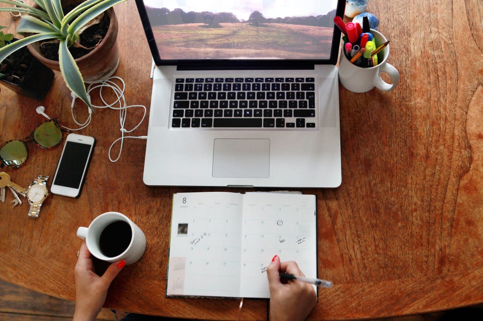 person writing in diary with laptop on desk