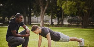 personal trainer instructing young man doing push ups in park