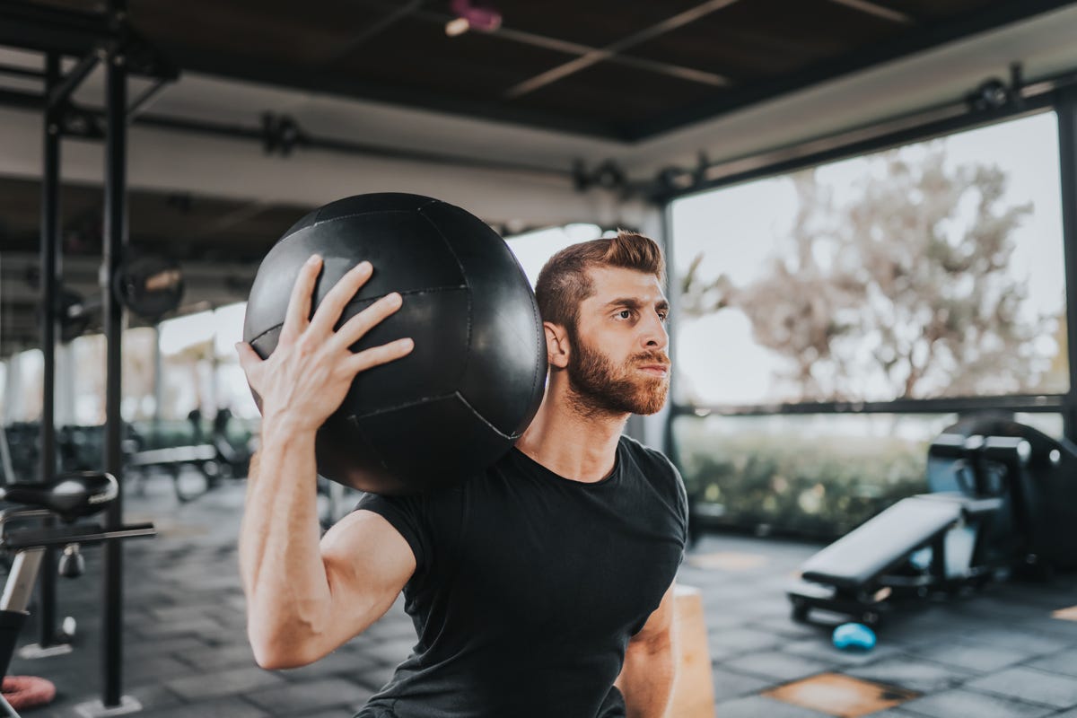 Hombre en ropa deportiva haciendo ejercicio con un balón medicinal crossfit  en un gimnasio