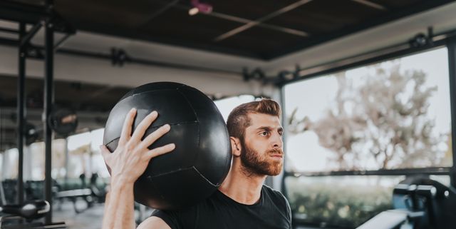 Hombre en ropa deportiva haciendo ejercicio con un balón medicinal crossfit  en un gimnasio