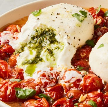 pesto stuffed burrata on top of burst cherry tomatoes with basil