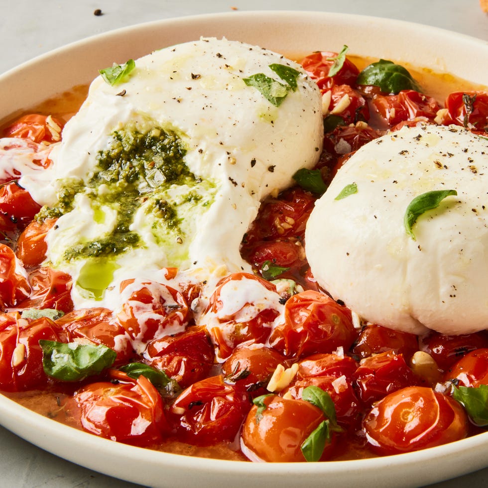 pesto stuffed burrata on top of burst cherry tomatoes with basil