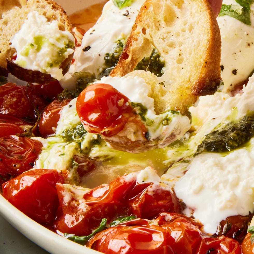 pesto stuffed burrata on top of burst cherry tomatoes with basil