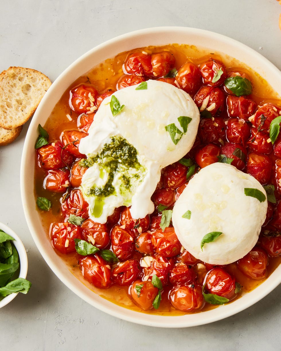 pesto stuffed burrata on top of burst cherry tomatoes with basil