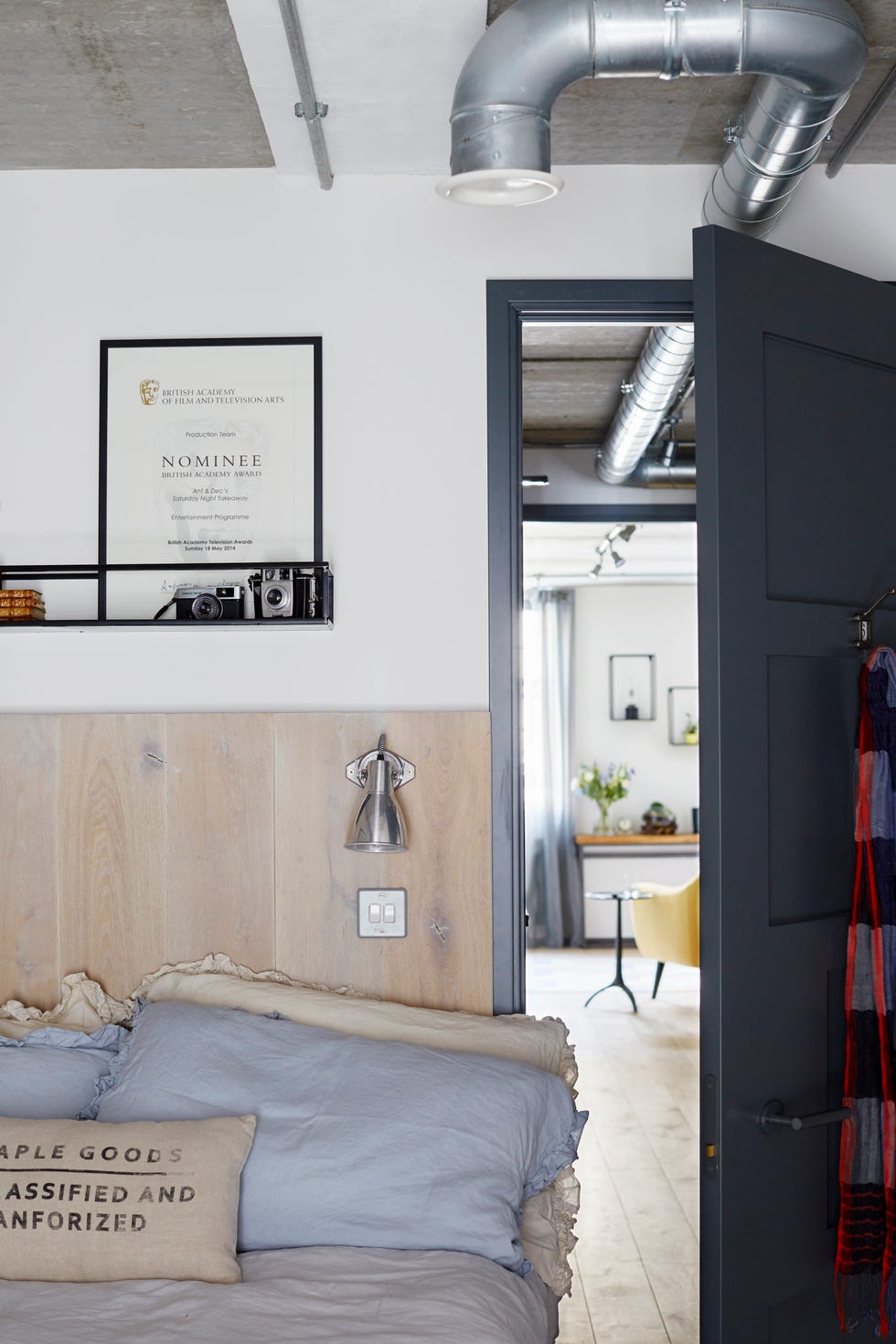 a wooden bed frame in a white bedroom with silver pipes on the ceiling and a framed award above the bed