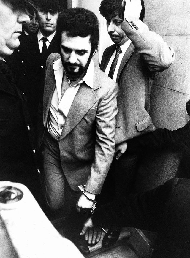 peter sutcliffe looking downward amid a crowd of people as he is led in handcuffs to court