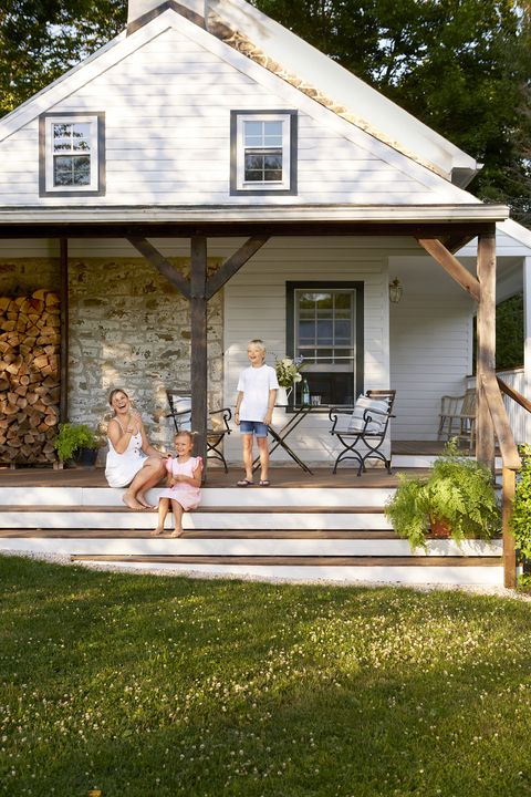 a mom and a boy and girl sit on the porch steps of a country house