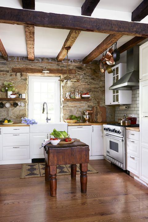 stone walls and wooden ceiling beams and hardwood floors in a kitchen with a dark wood butcher block
