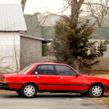 a red peugeot 505 v6 stx parked in front of a house