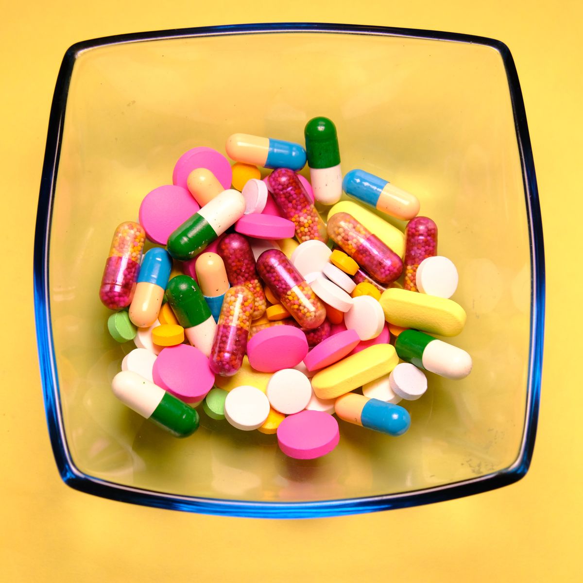 pharmaceutical medicine pills, tablets and capsules in bowl on yellow background