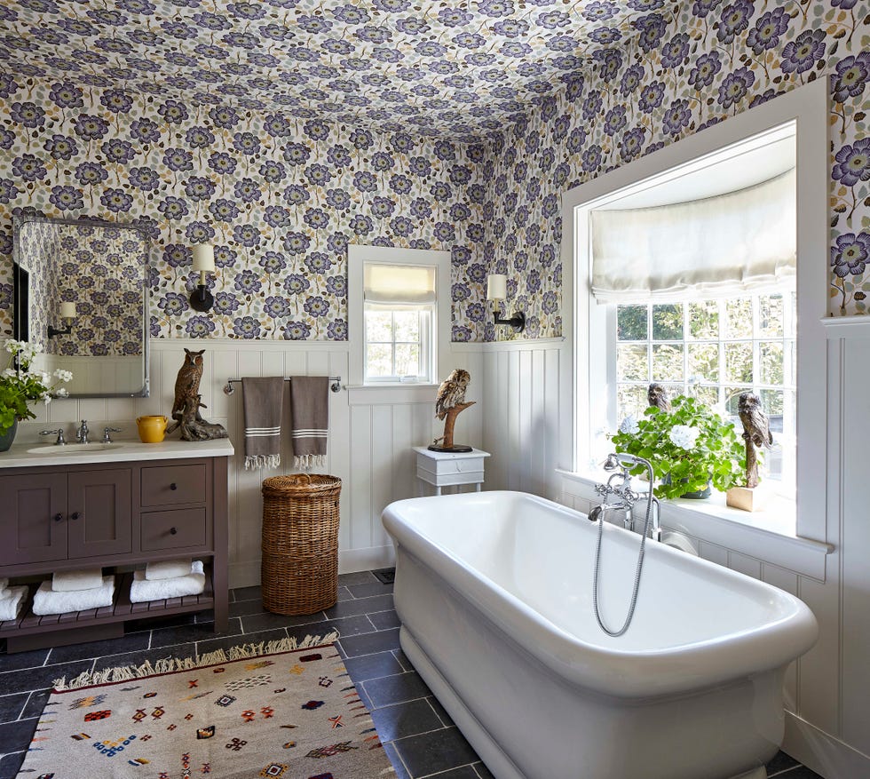 the upper walls and ceiling are covered in a flowery wallpaper and there is a soaking tub under the window