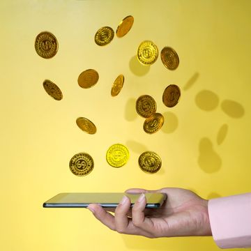smartphone in hand met geldmunten die erop vallen voor gele achtergrond