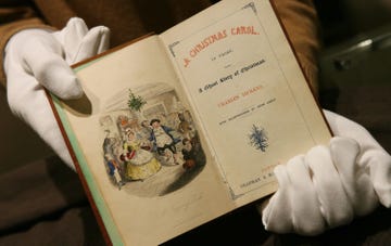 a vintage book titled a christmas carol held in gloved hands featuring an illustration on the left page