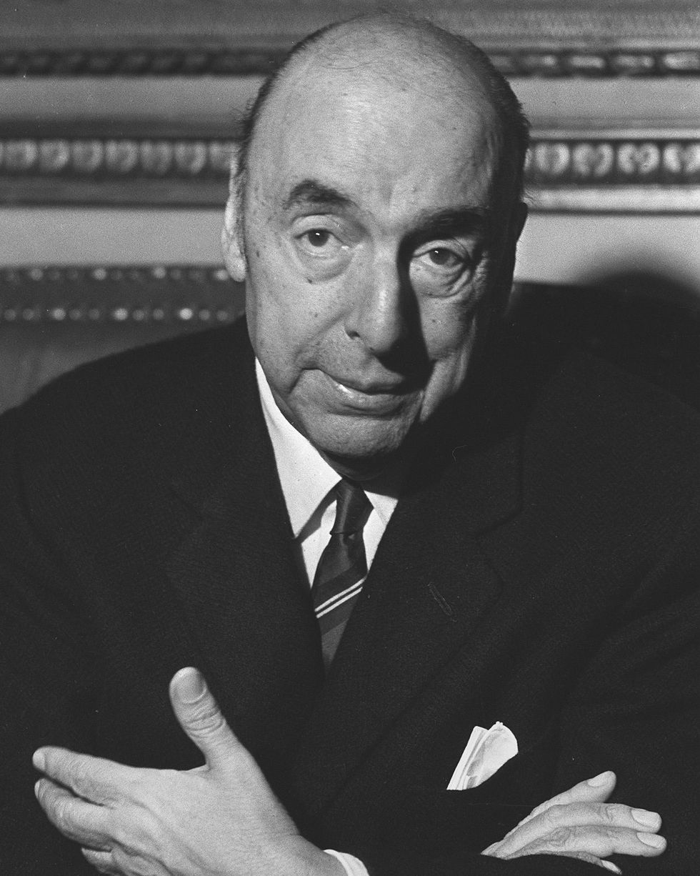 pablo neruda crossing his hands and looking straight ahead as he sits in a chair