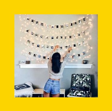 a woman hanging photos with string and fairy lights above a shelf wearing a grey jumper and denim shorts