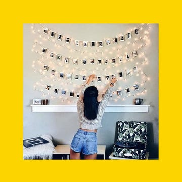 a woman hanging photos with string and fairy lights above a shelf wearing a grey jumper and denim shorts