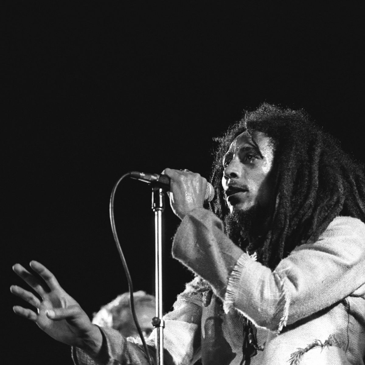 bob marley holding a microphone with his left hand and looking out toward an audience as he sings
