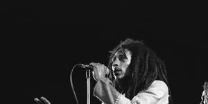 bob marley holding a microphone with his left hand and looking out toward an audience as he sings