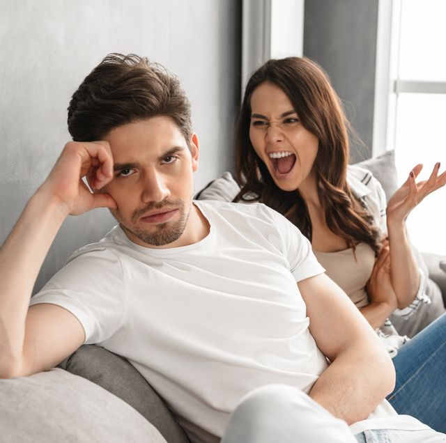disappointed couple sitting together on sofa at home with upset look while woman screaming on man, isolated over white background