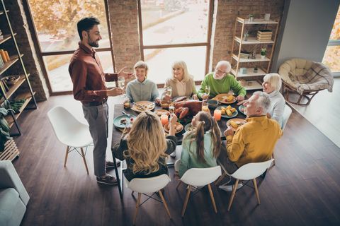 full big family gathering sit feast meals dinner table father guy tell thanksgiving pray toast multi generation eight members in evening living room indoors
