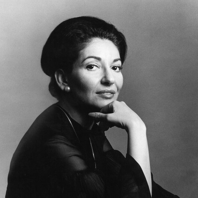 maria callas looks at the camera in a studio portait with her chin resting on the back of one of her hands, she wears a long sleeve blouse with a silver chain necklace and pearl stud earrings