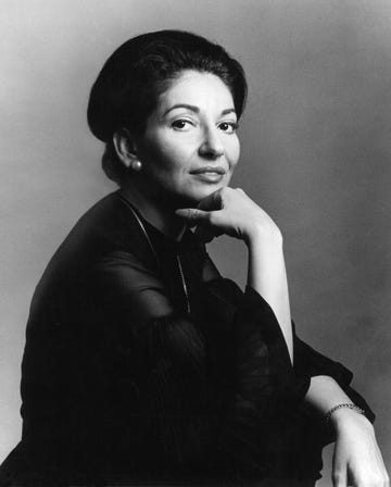 maria callas looks at the camera in a studio portait with her chin resting on the back of one of her hands, she wears a long sleeve blouse with a silver chain necklace and pearl stud earrings