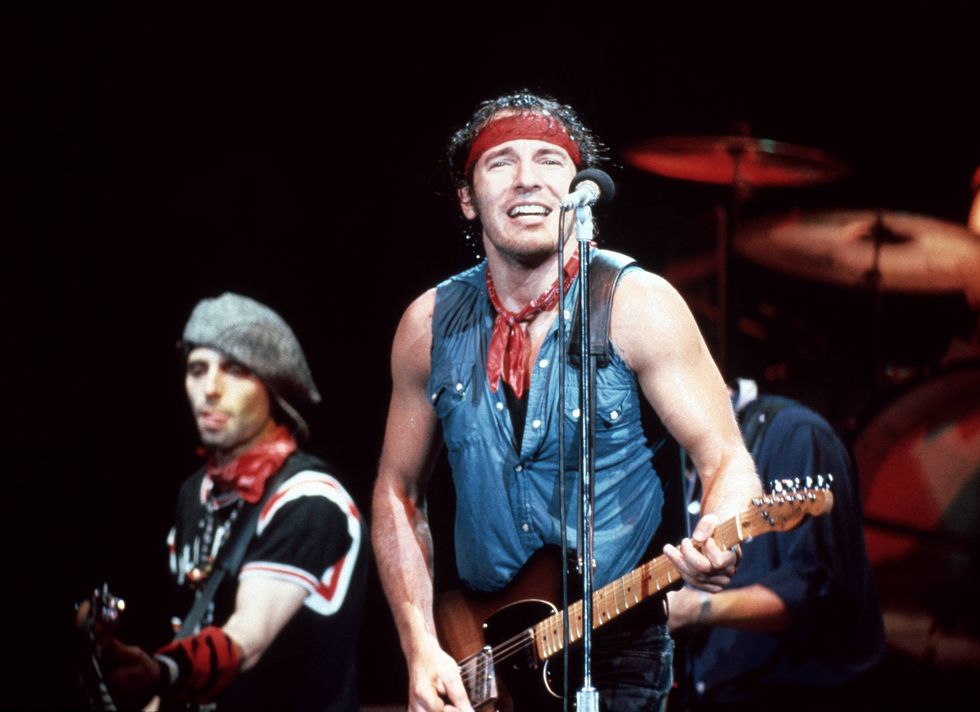 bruce springsteen standing behind a stage microphone and playing the guitar during a concert