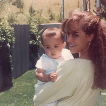 young mother posing holding her son looking at the camera at her home backyard
