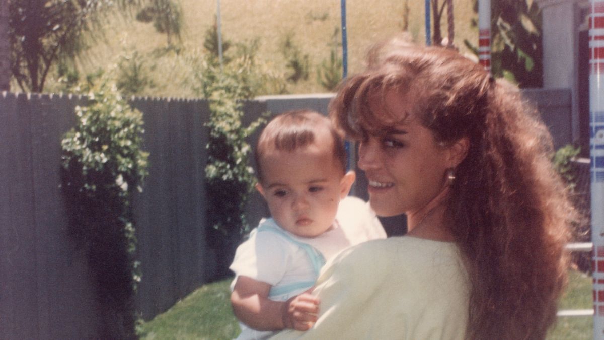 young mother posing holding her son looking at the camera at her home backyard