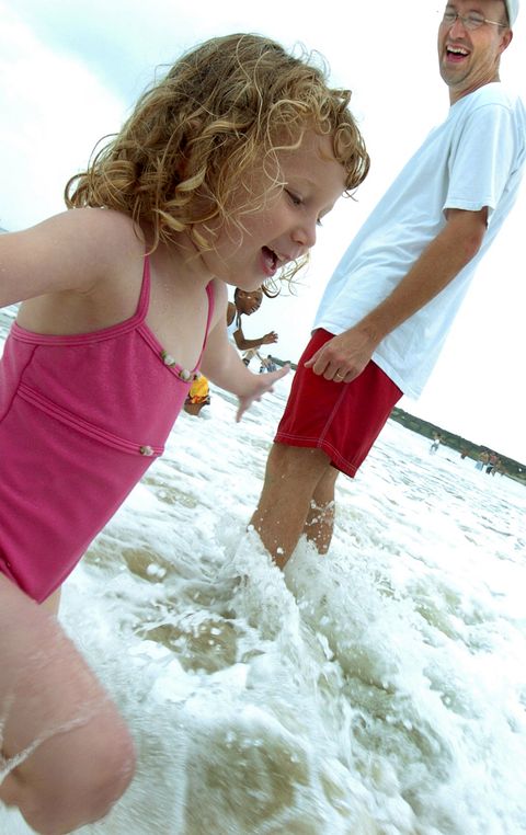 young girl smiles with her feet in the surf as dad beside her laughs