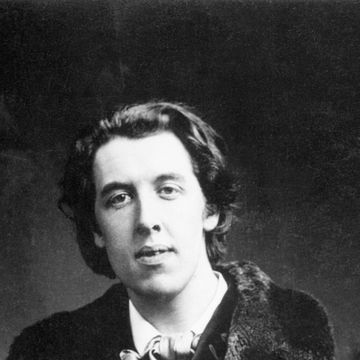 a man in a fur trimmed long coat and suit looks at the camera while standing for a photo