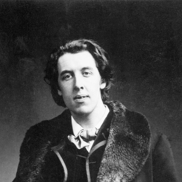 a man in a fur trimmed long coat and suit looks at the camera while standing for a photo