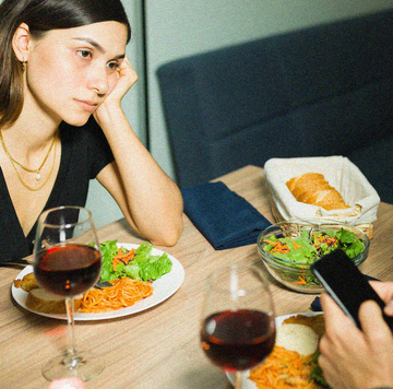 young girlfriend looking annoyed at her busy boyfriend texting on his smartphone during a dinner date