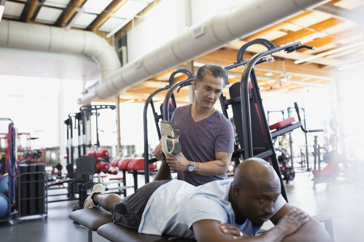Physical therapist stretching patient leg at gym