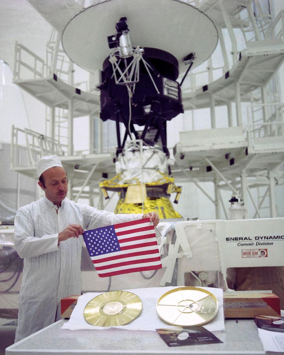 a photo of voyager, the golden record, and an american flag held by project manager john casani