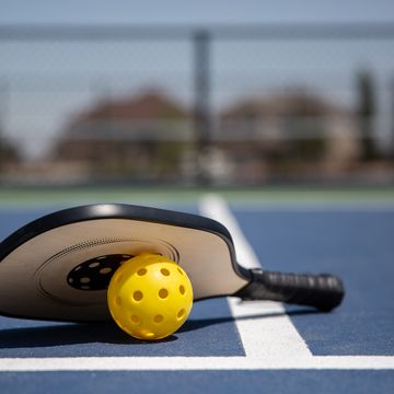 a pickleball paddle and yellow ball on a court