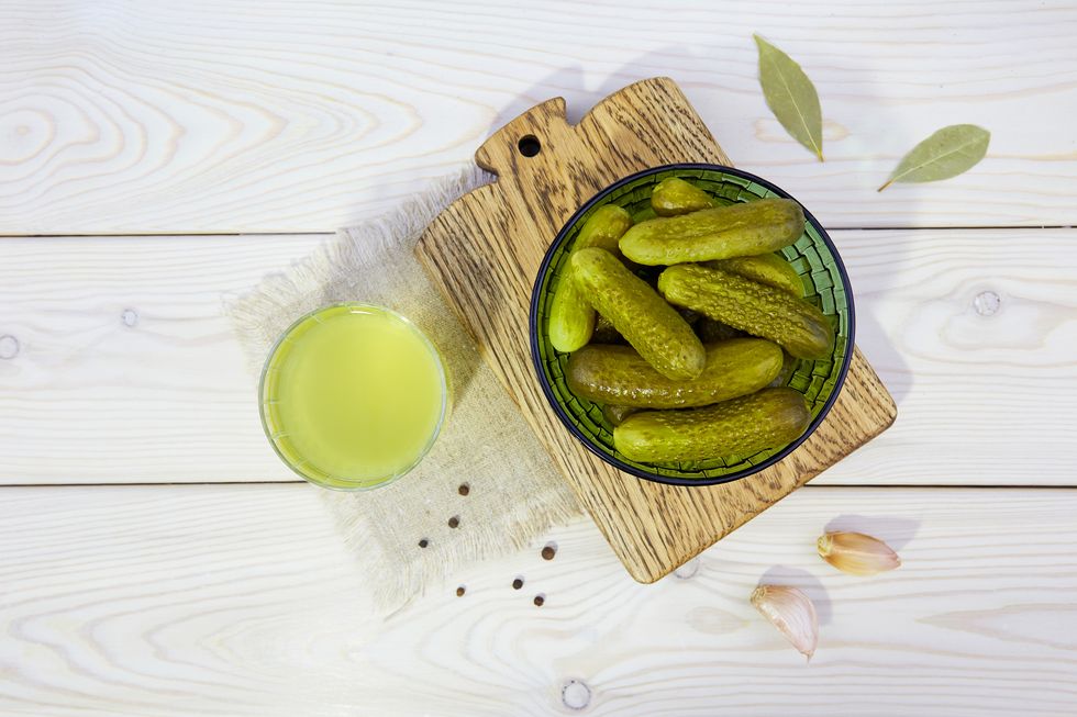 pickled cucumbers in a ceramic bowl, pickle juice in glass on a white wooden background. homemade marinated gherkins.